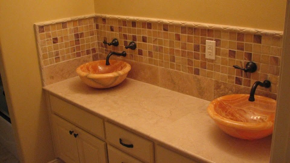 Bathroom vanity with two orange vessel sinks, dark faucets, and beige tile backsplash