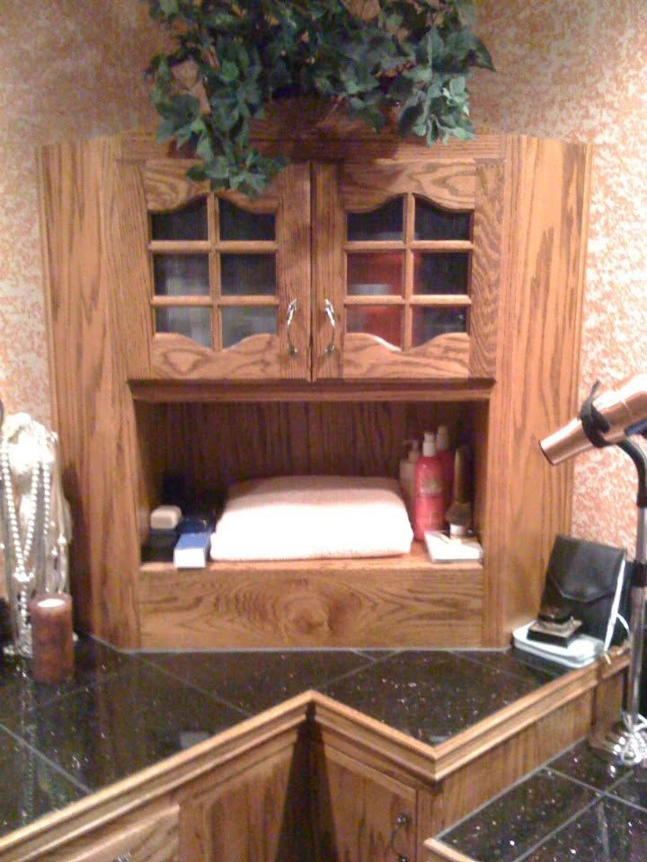 Wooden bathroom vanity with open shelf, sink area, and green plants on top against a tiled wall