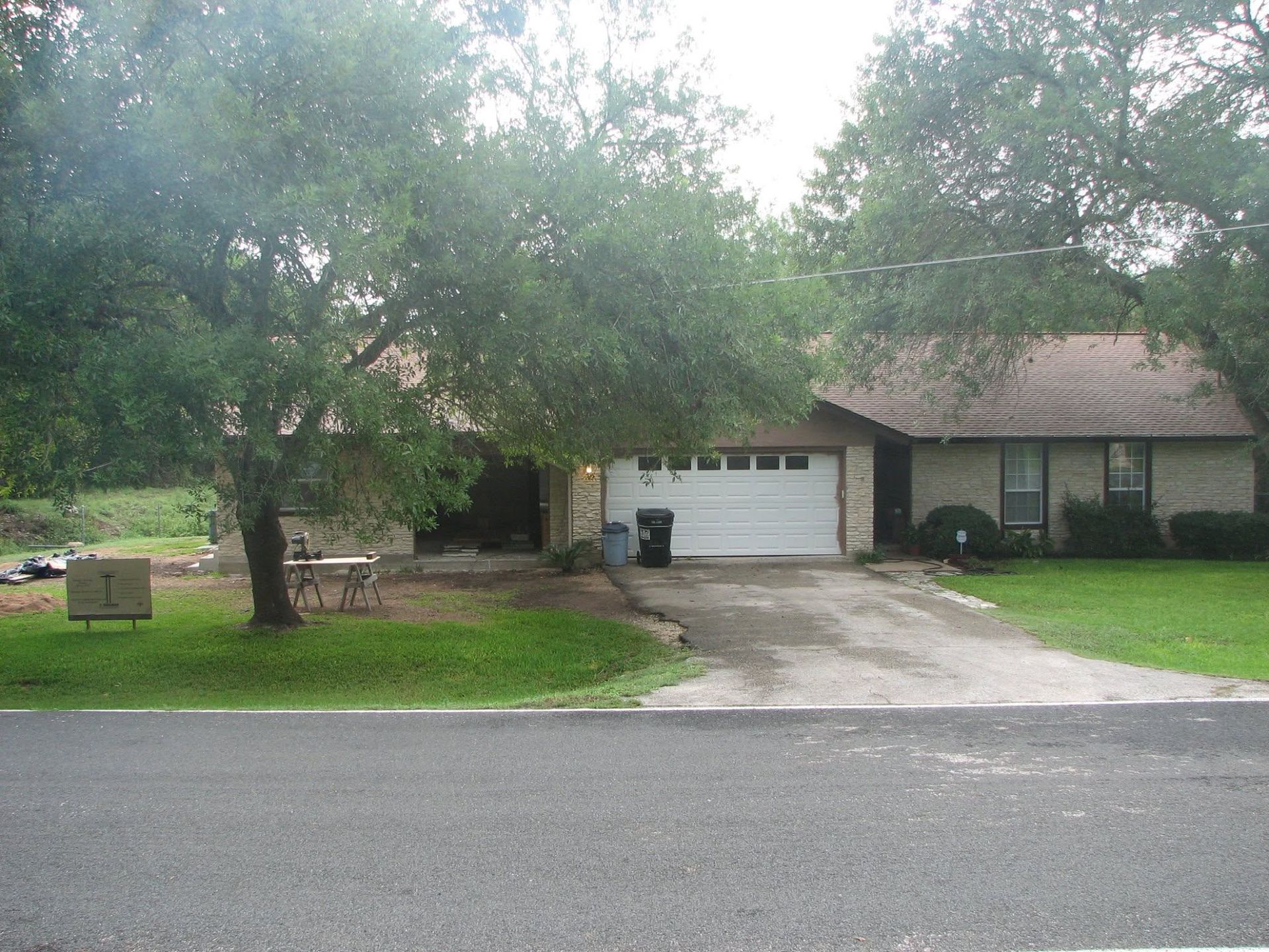 Suburban house with a two-car garage, trees in front, and a driveway beside the street