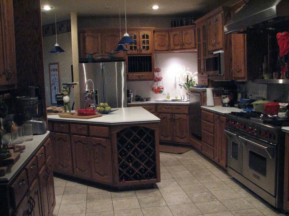 Warm kitchen with wood cabinets, stainless appliances, tiled floor, and a central island under soft lighting