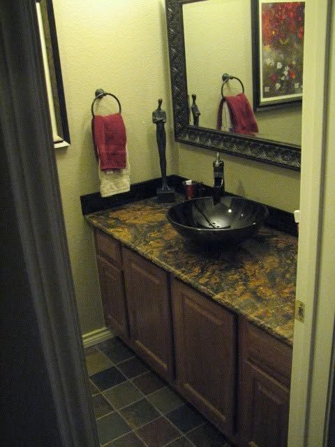 Small bathroom vanity with dark wood cabinets, black vessel sink, granite counter, and red hand towel.