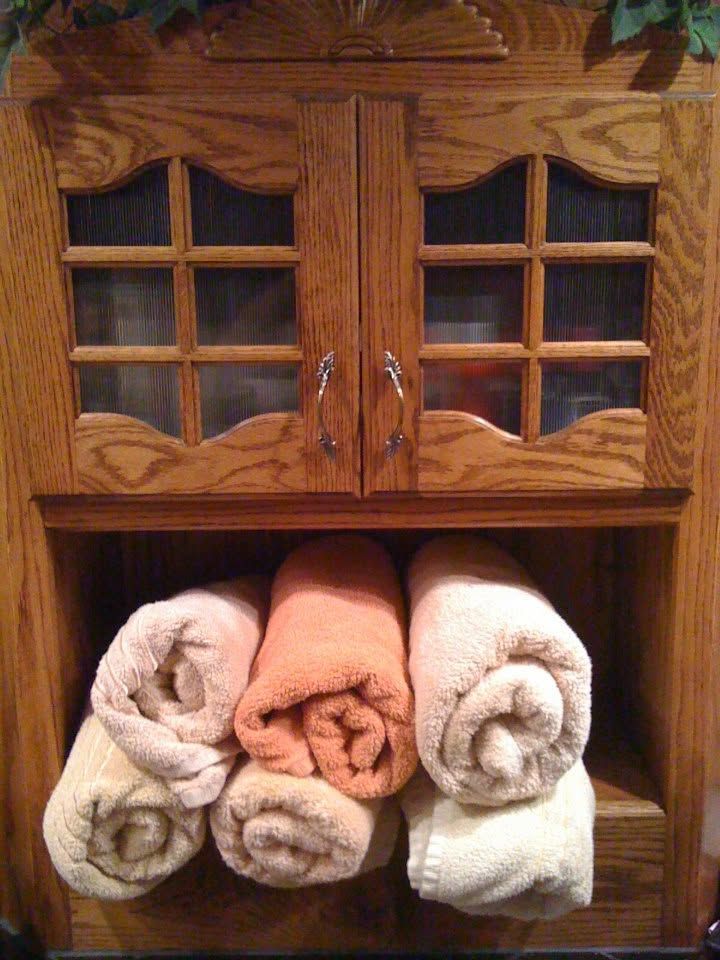 Wooden cabinet with glass doors above and rolled towels in white, peach, and beige below