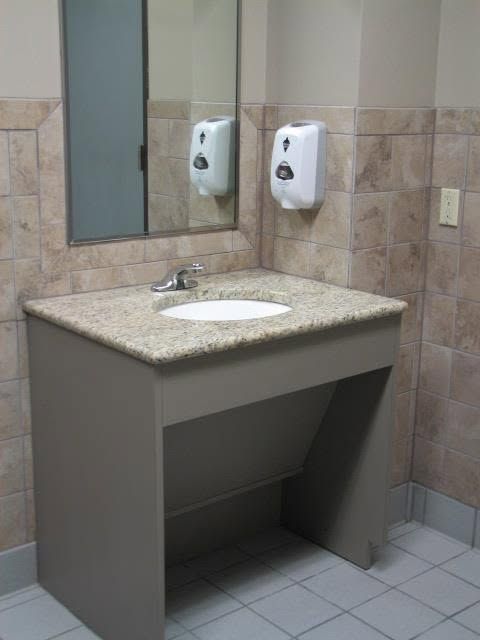 Accessible bathroom sink with granite countertop, mirror, and wall-mounted soap dispensers
