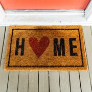 “HOME” doormat with a red heart on a porch, in front of a red door