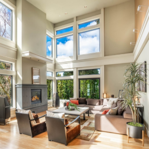 Bright modern living room with tall windows, fireplace, and light wood floors, furnished with neutral sofas and chairs