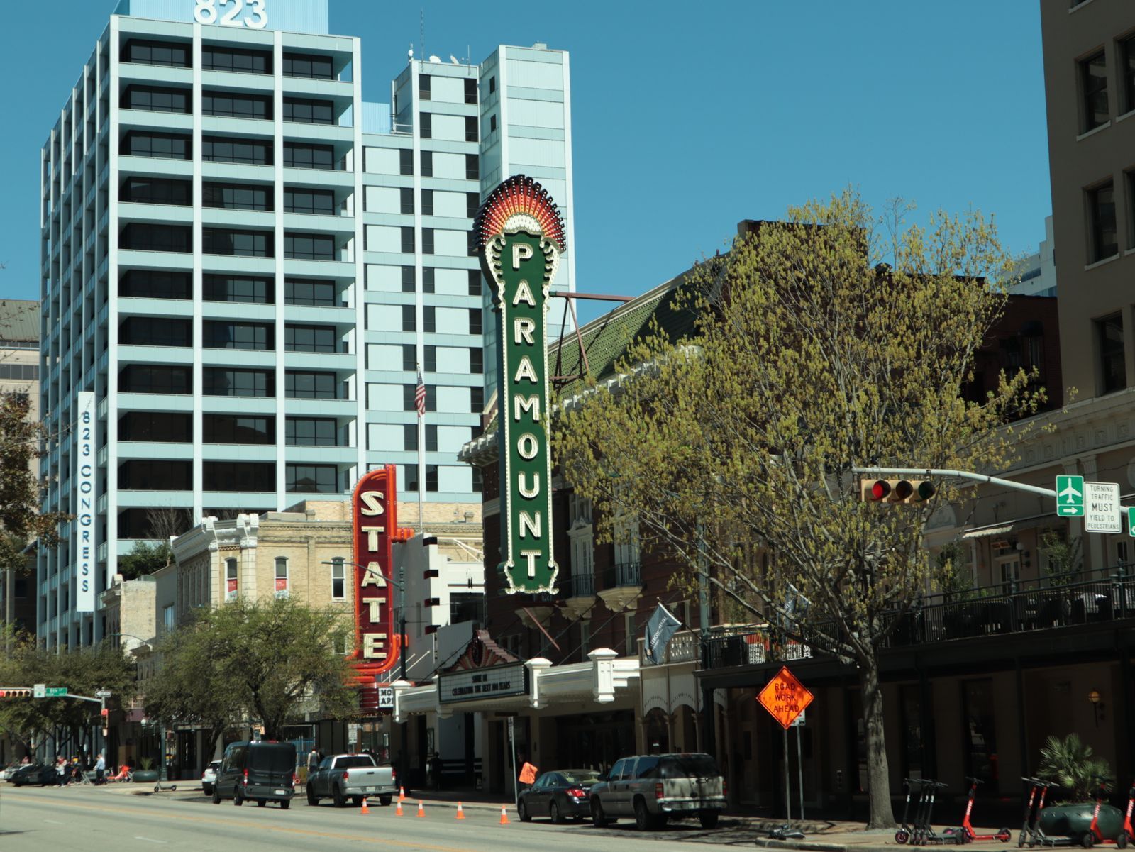 Downtown street with the Paramount theater marquee beside tall modern buildings under a clear blue sky