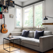 Cozy living room with gray sofa, wall shelves of books, acoustic guitar, and large window light