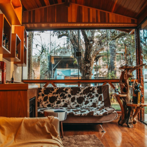 Cozy wooden living room with a cowhide sofa, warm lighting, and large windows opening to trees outside