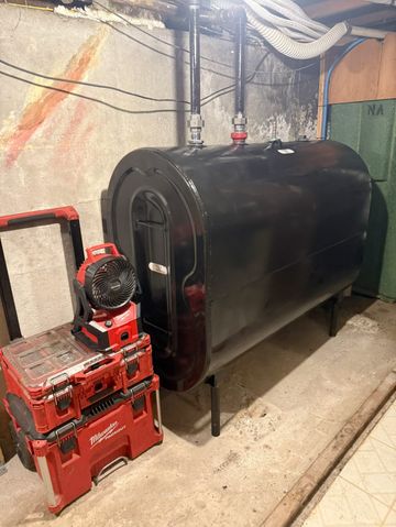 Black oil tank in a basement, with red Milwaukee toolboxes and work light nearby.