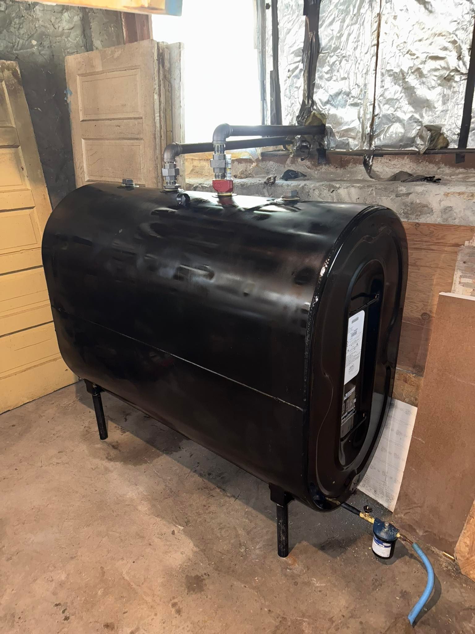 Black oil tank with pipes and gauge in a basement.