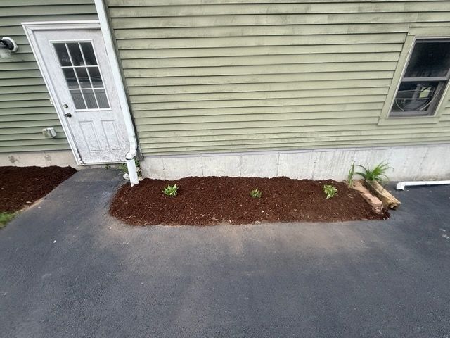 Side of a beige house with a white door, small windows, and a fresh mulch bed along the foundation.