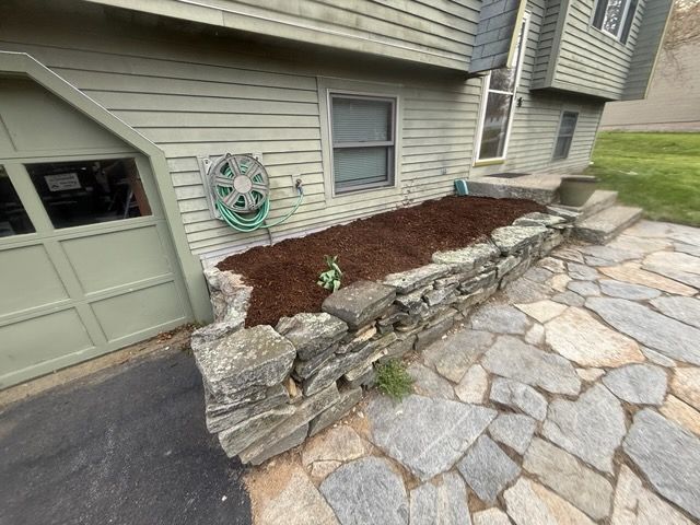 Stone retaining wall beside house with garage, flagstone patio, and mulched garden bed
