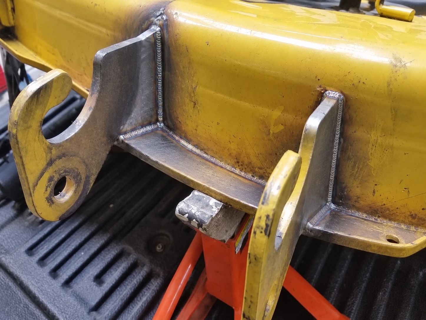 Yellow industrial machine bracket with metal mounting tabs and a red support underneath