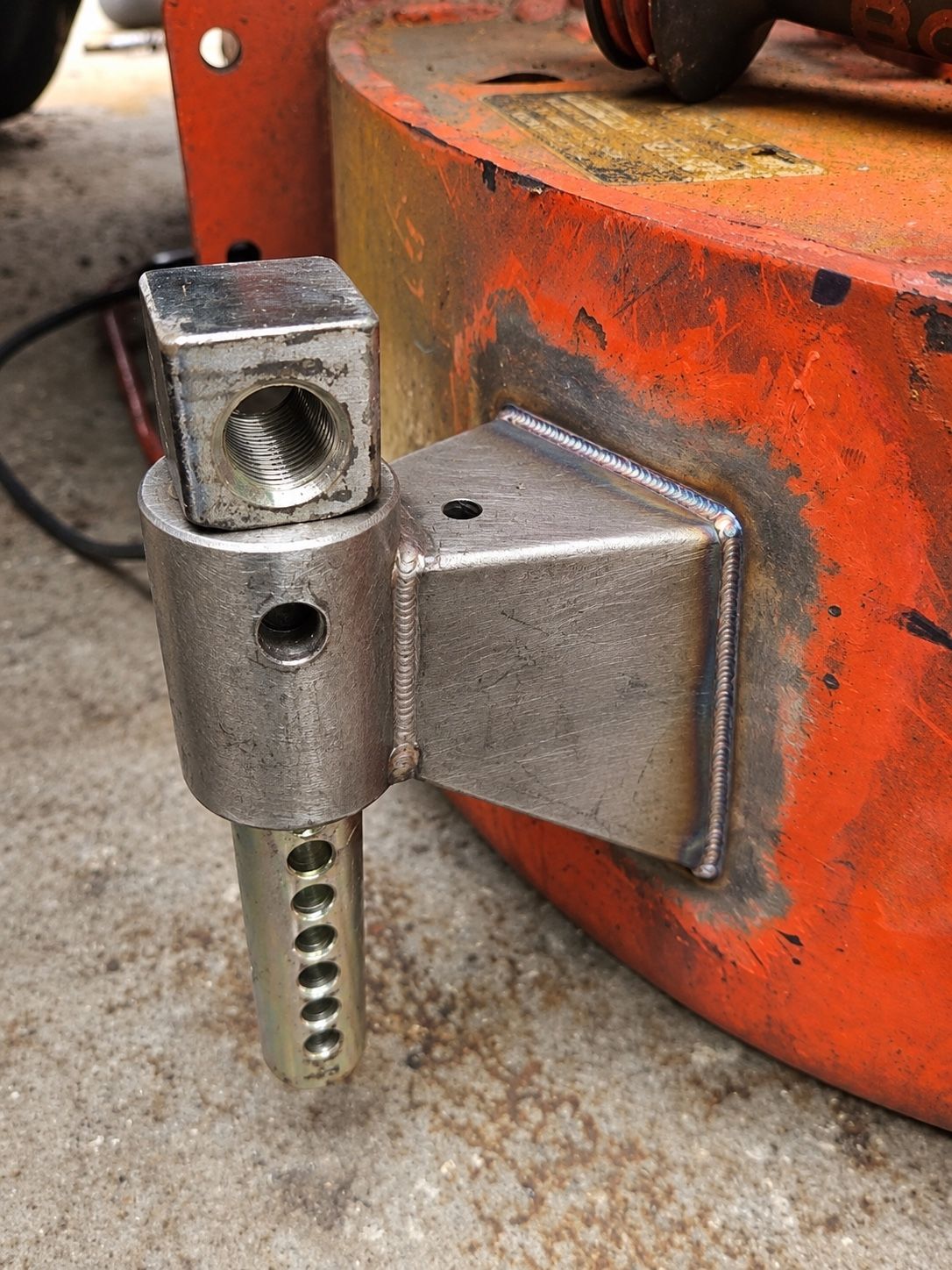 Metal hinge clamp attached to an orange machine base on a concrete floor