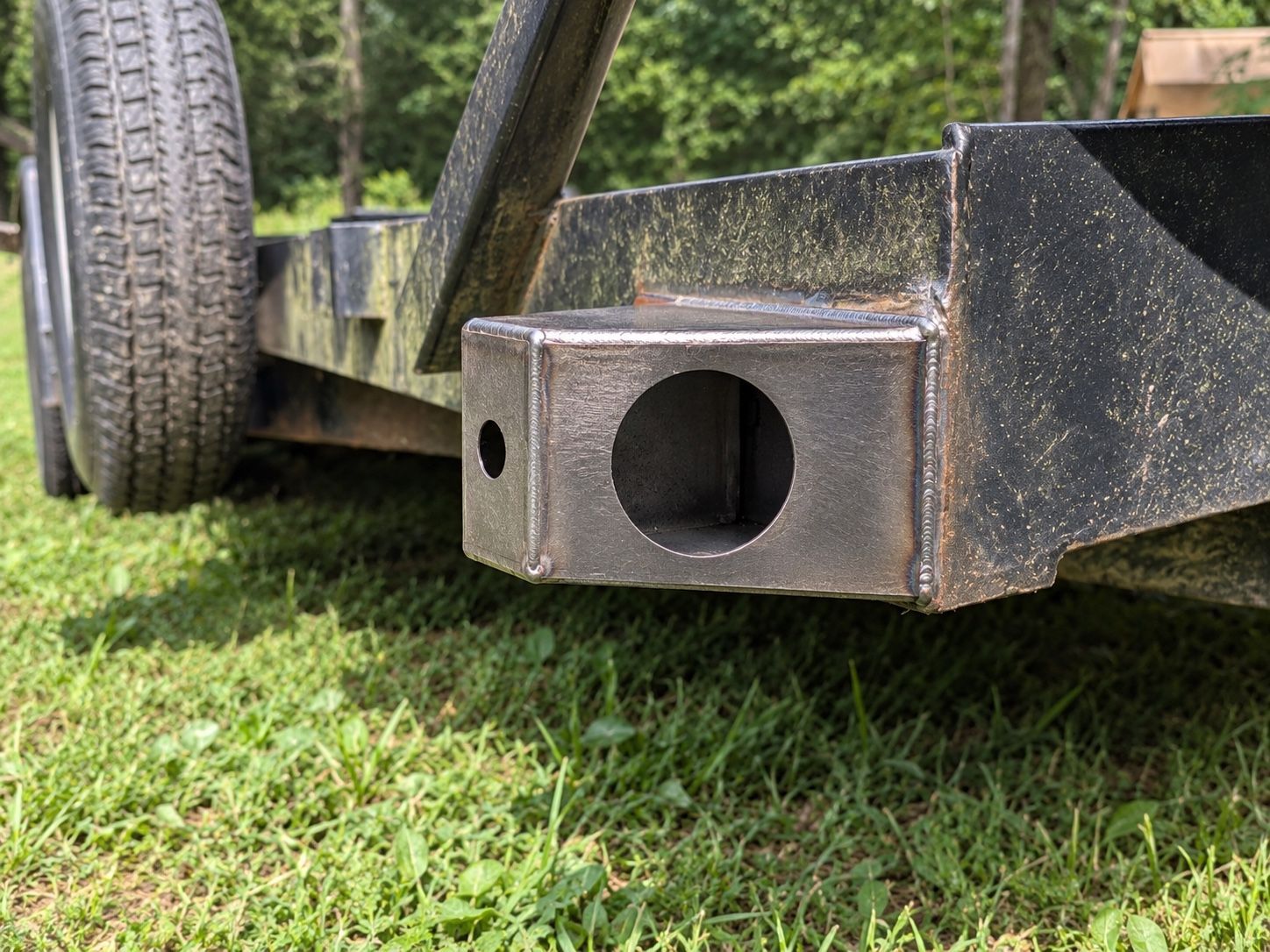 Close-up of a black trailer hitch receiver on a wheeled metal trailer over grass.