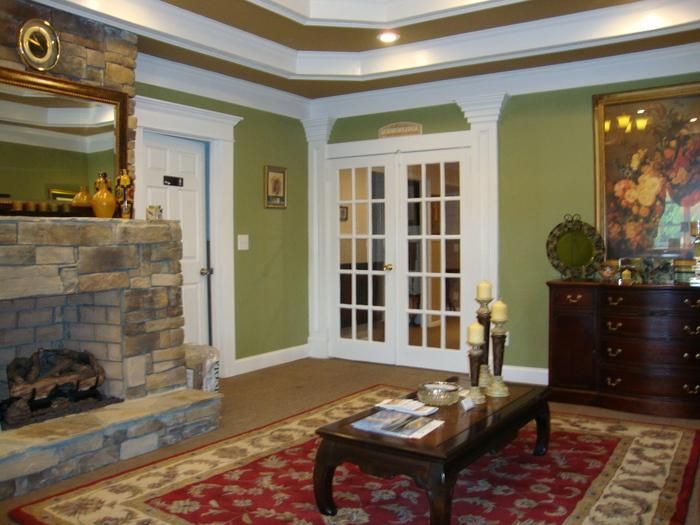 Cozy living room with stone fireplace, green walls, French doors, and red patterned rug