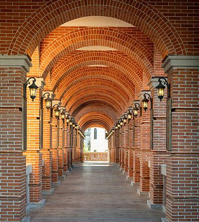 A long, symmetrical brick archway lined with glowing wall lamps, leading to an open outdoor space. A long, symmetrical brick archway lined with glowing wall lamps, leading to an open outdoor space.