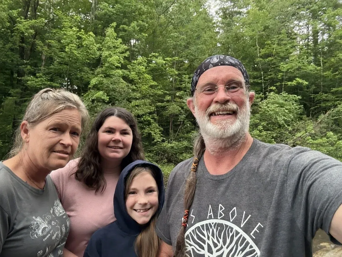 Four people smiling in a wooded outdoor setting, posing close together for a group selfie.