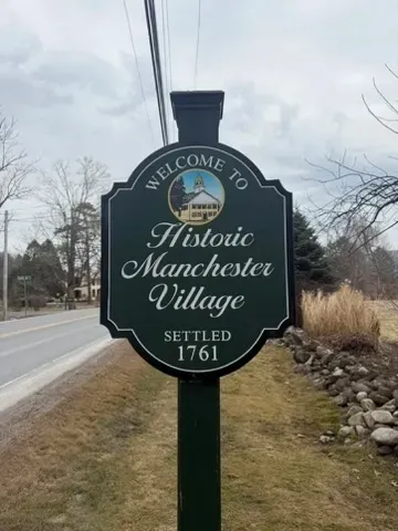 Historic Manchester Village welcome sign by roadside, reading “Welcome to Historic Manchester Village, Settled 1761.”