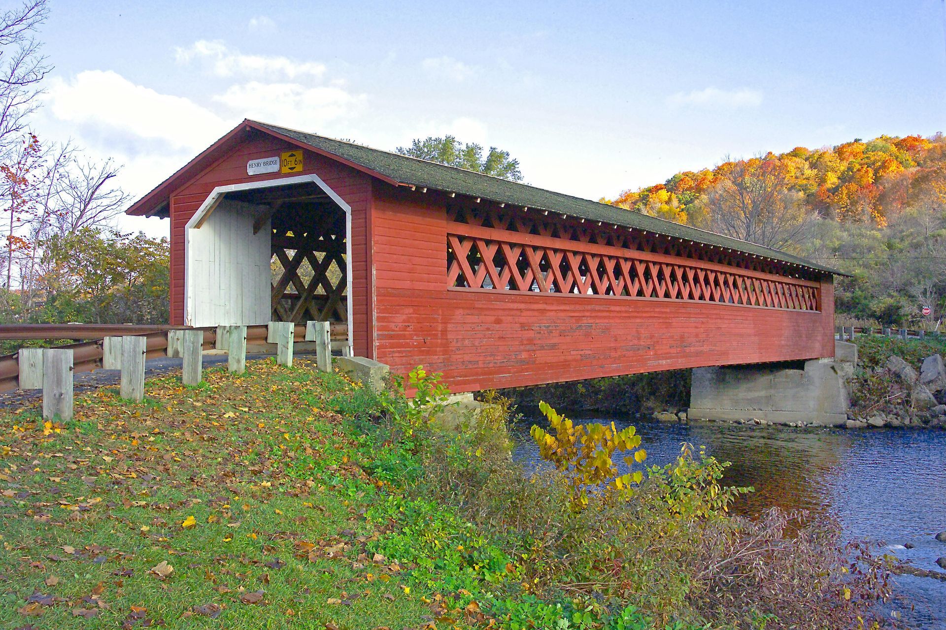 Red covered bridge over a river in a wooded autumn landscape