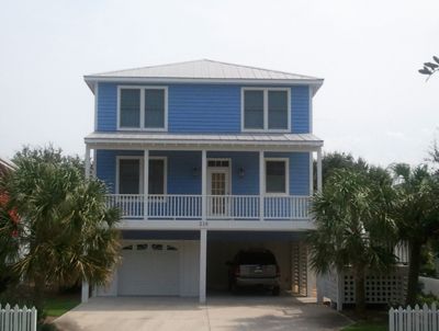 A blue house with a car parked underneath it