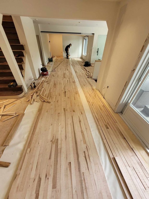Vue intérieure d'une longue pièce où l'on pose un parquet. Une personne travaille au fond de la pièce.