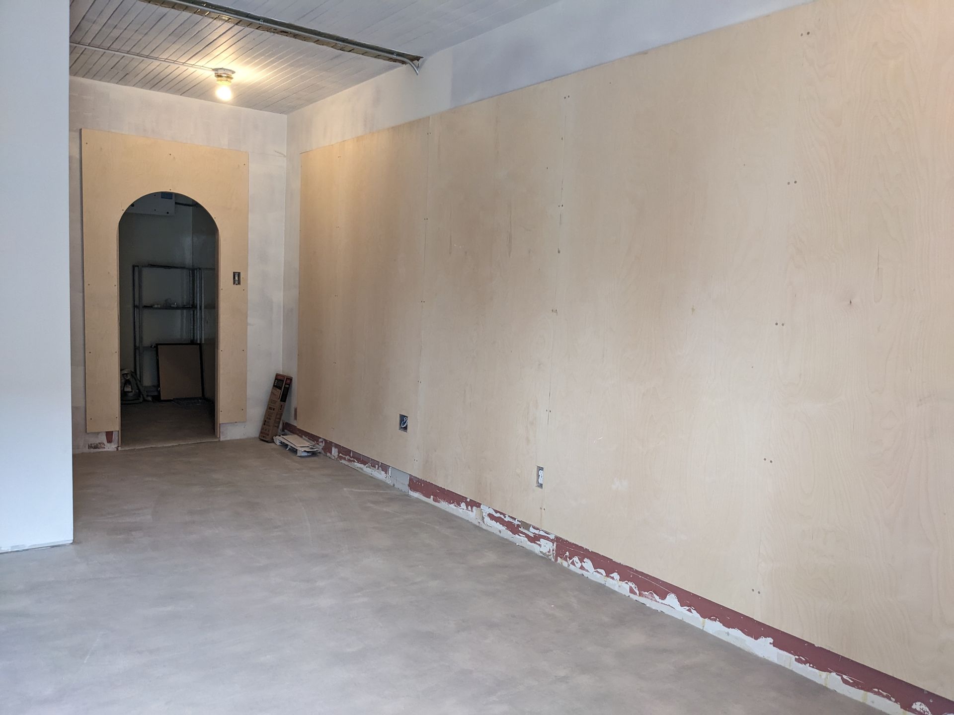 Une pièce vide aux tons clairs, en cours de rénovation. Les murs ne sont pas finis et une porte donne sur une autre pièce.