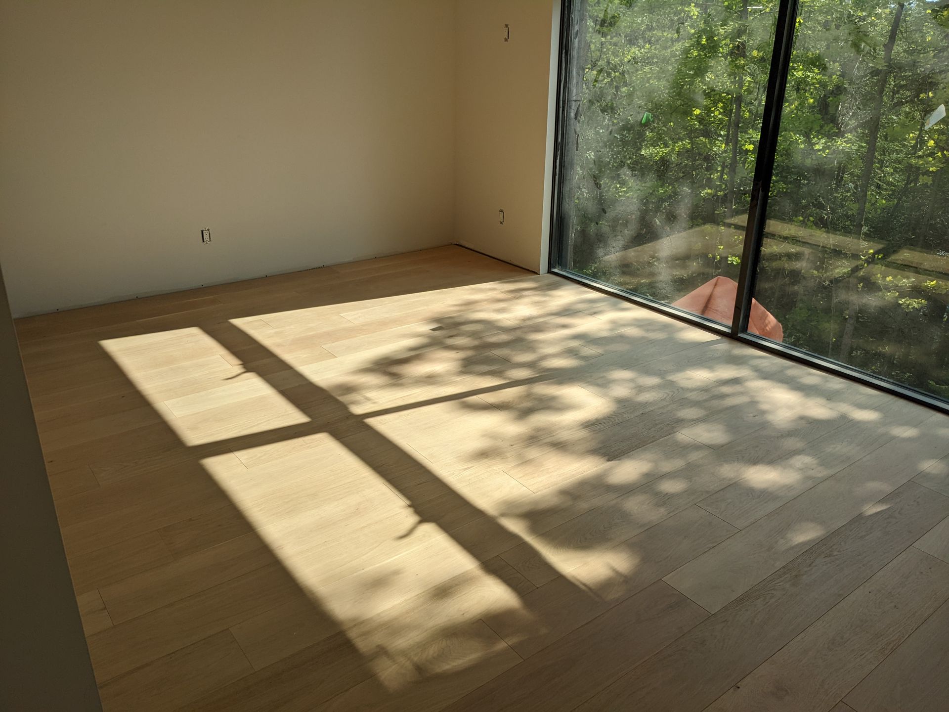 Pièce vide avec parquet clair et grande fenêtre projetant des ombres.
