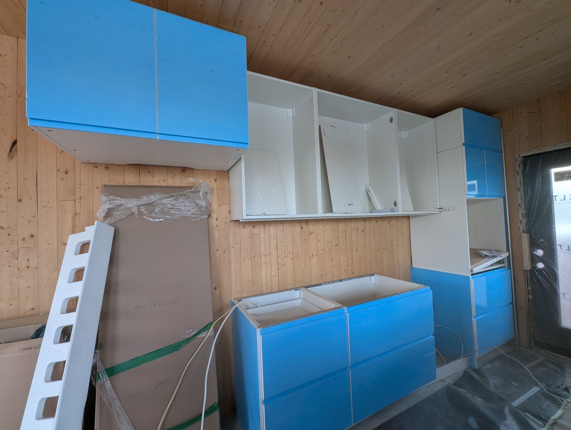Installation de meubles de cuisine bleus et blancs dans une pièce aux murs lambrissés.