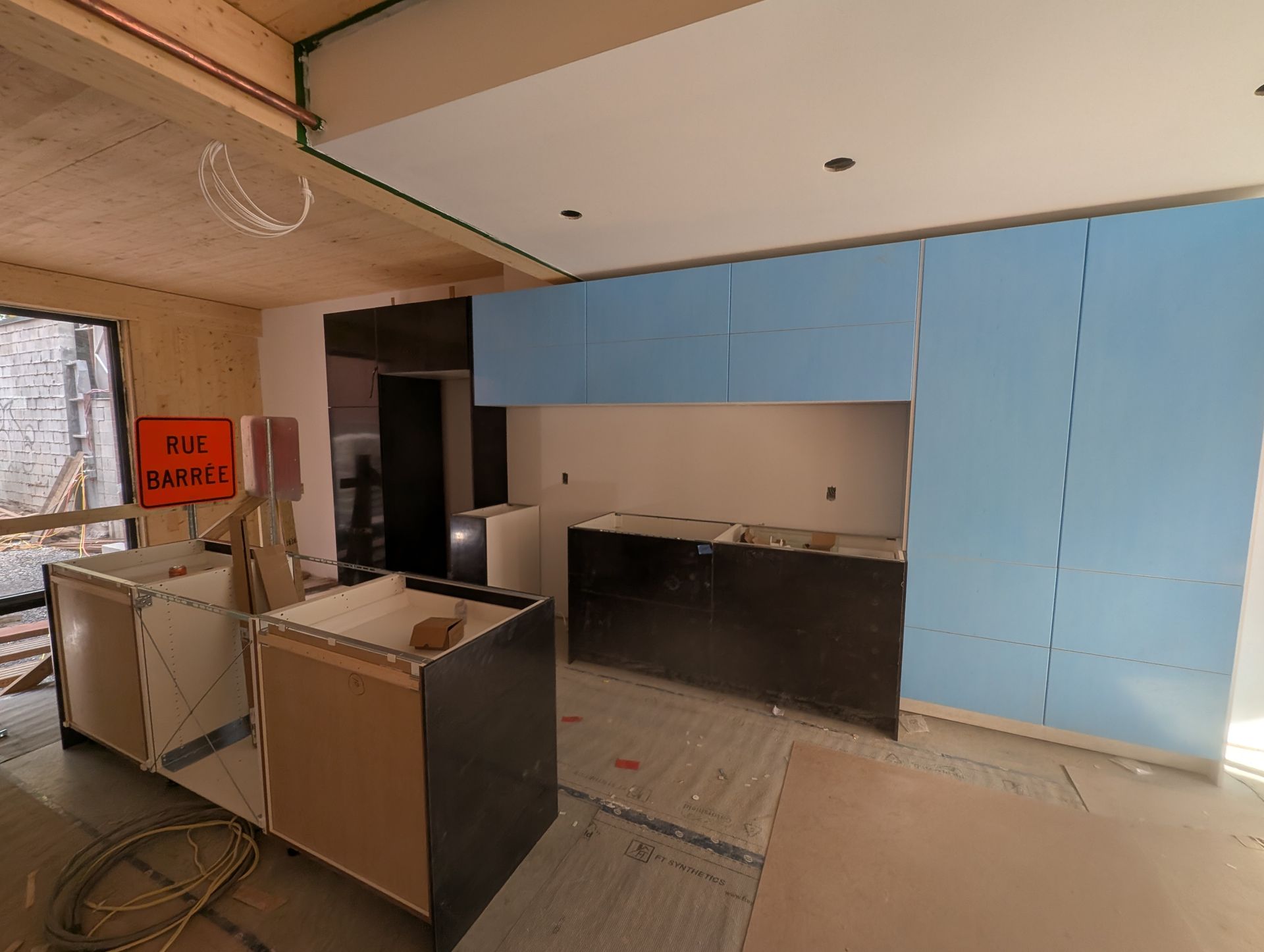 Cuisine en travaux avec des armoires bleues, des armoires et des murs non finis, et des panneaux de chantier.