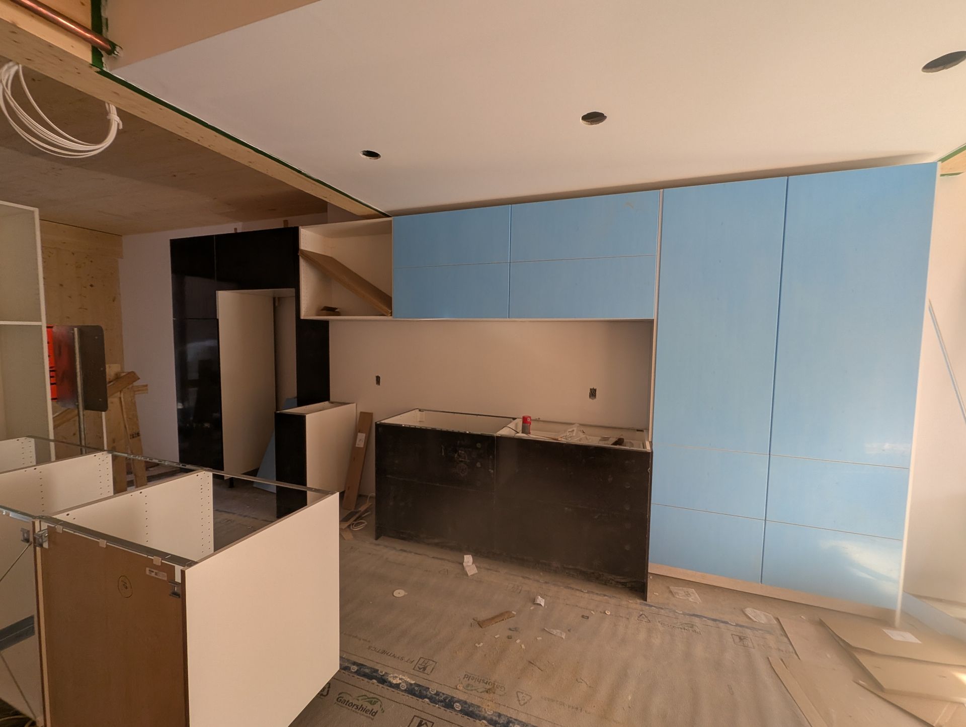 Cuisine en construction, avec des armoires bleues, un comptoir noir et des armoires et murs non finis.