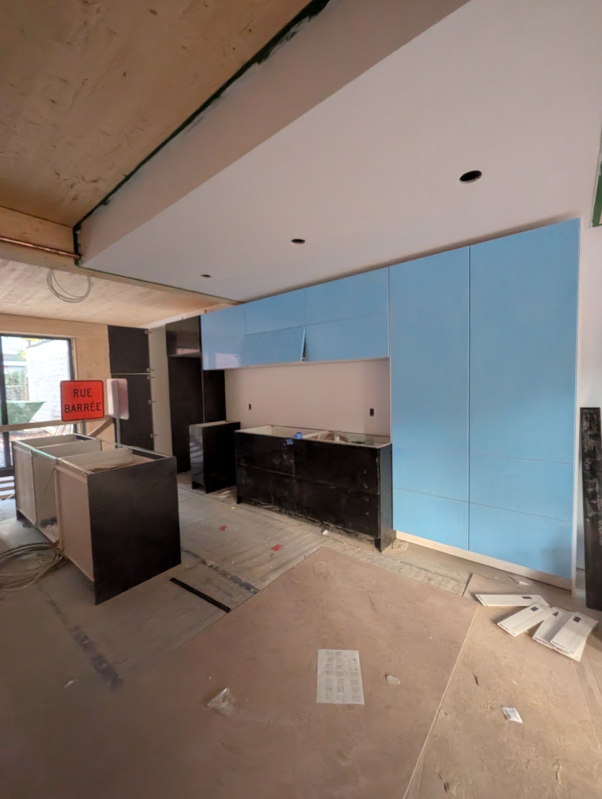 Cuisine en construction avec placards bleus et noirs, plafond clair et poutres apparentes.