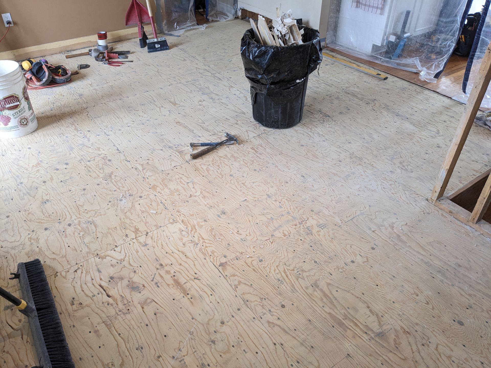 À l'intérieur, un sol en bois clair jonché de débris de construction, d'outils et d'un sac-poubelle.
