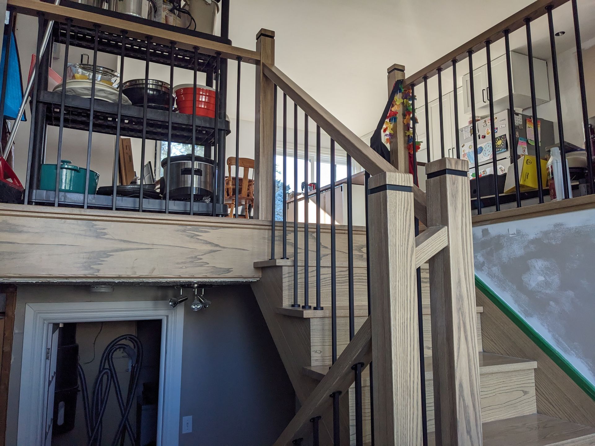 Un escalier en bois mène à une mezzanine avec une rambarde en métal ; une cuisine est visible en arrière-plan.