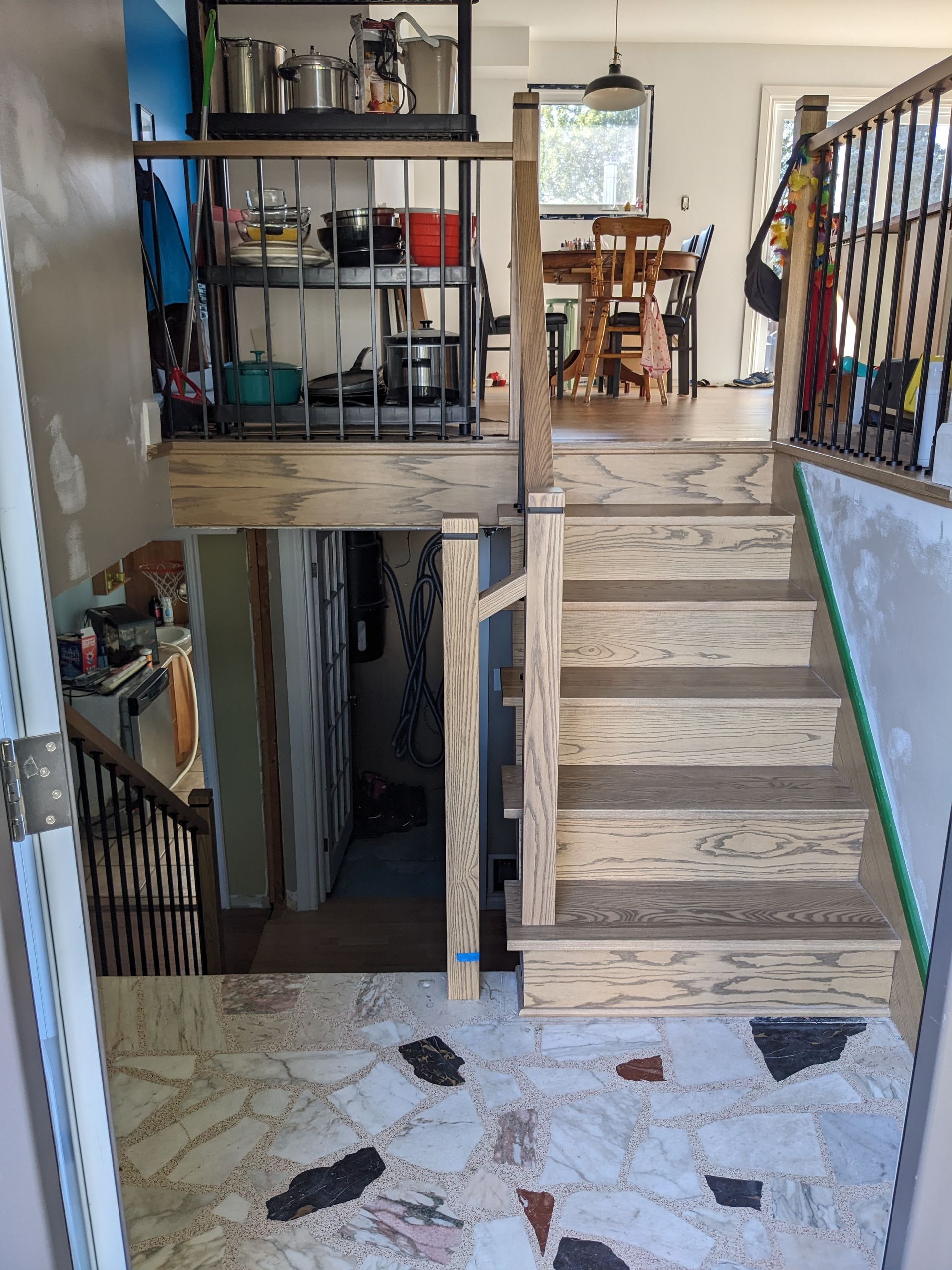 Escalier avec marches et rampe en bois menant à une cuisine avec étagères et un coin repas visible.