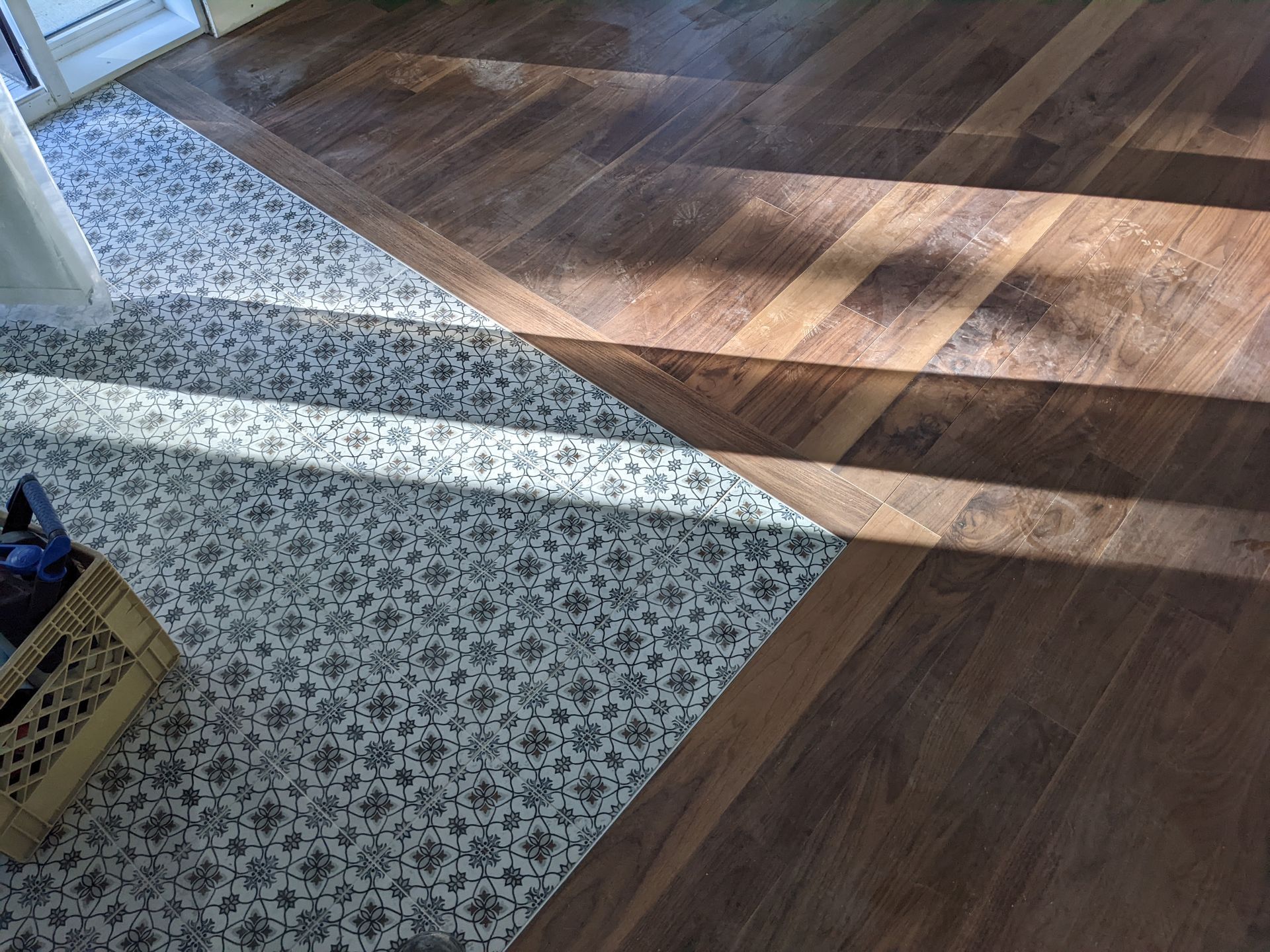 Sol carrelé avec une section à motifs et des lames de bois foncé posées en diagonale. Lumière naturelle traversant le sol.