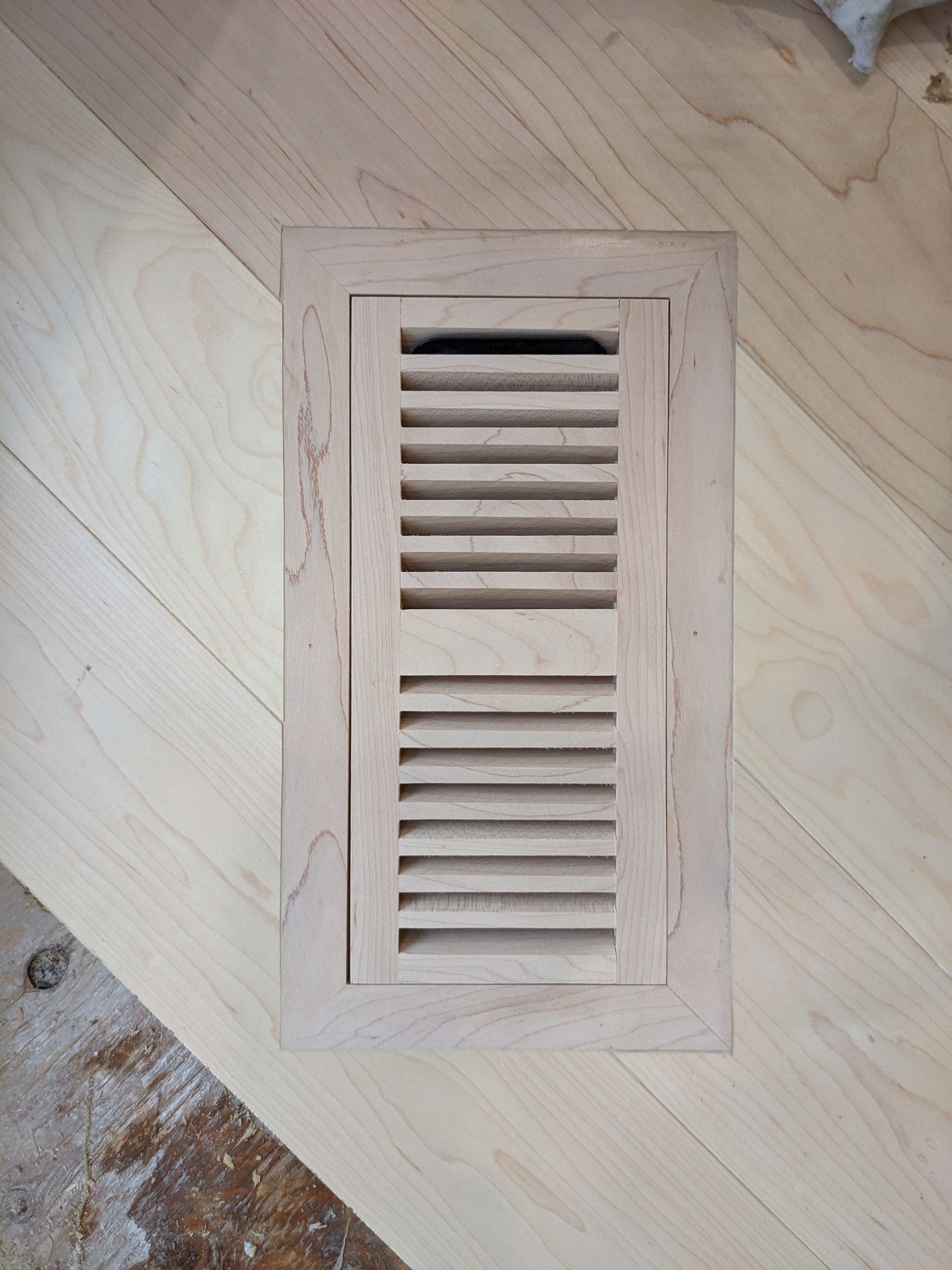Grille d'aération en bois à lattes horizontales, posée sur un parquet clair.