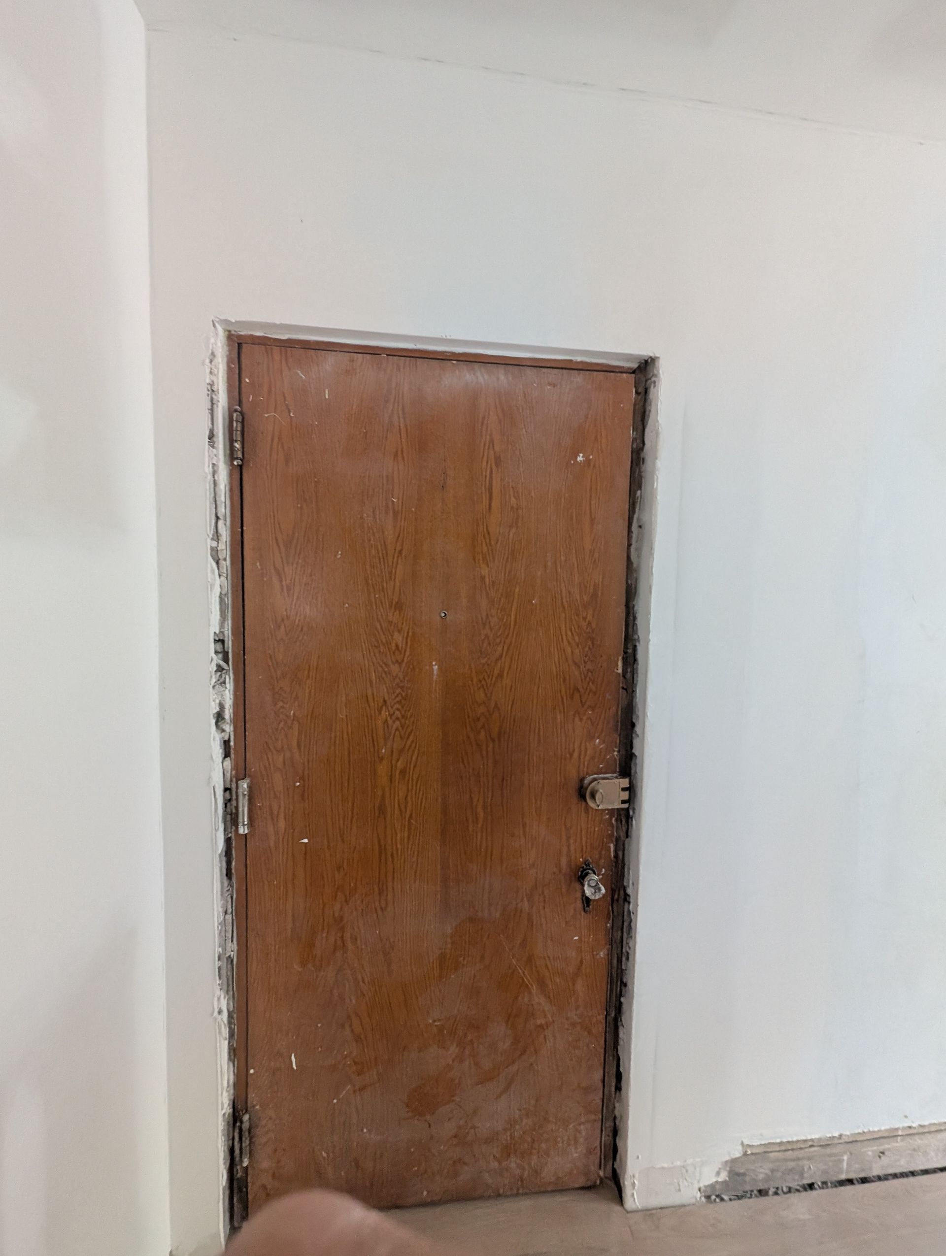 Porte marron encastrée dans un mur blanc, charnières et serrure apparentes.