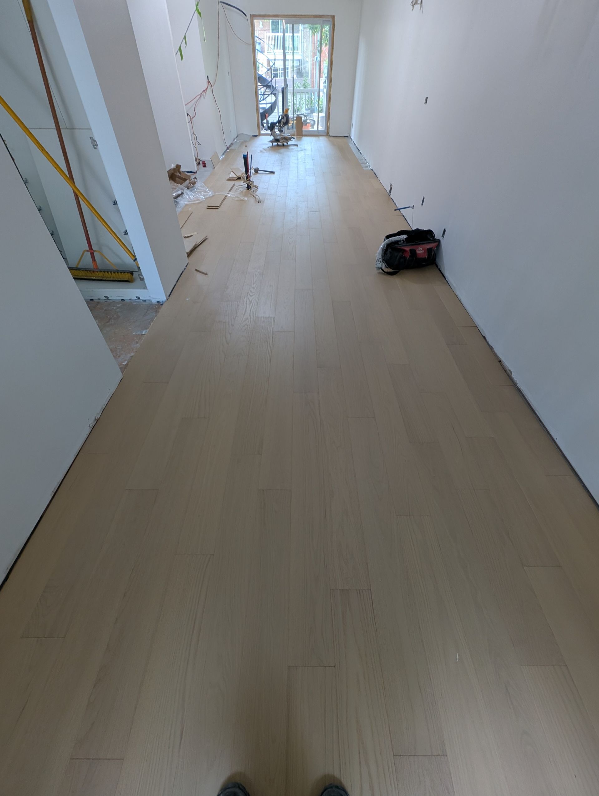 Parquet clair récemment installé dans une pièce longue et étroite aux murs blancs, avec des outils de construction et une porte ouverte.