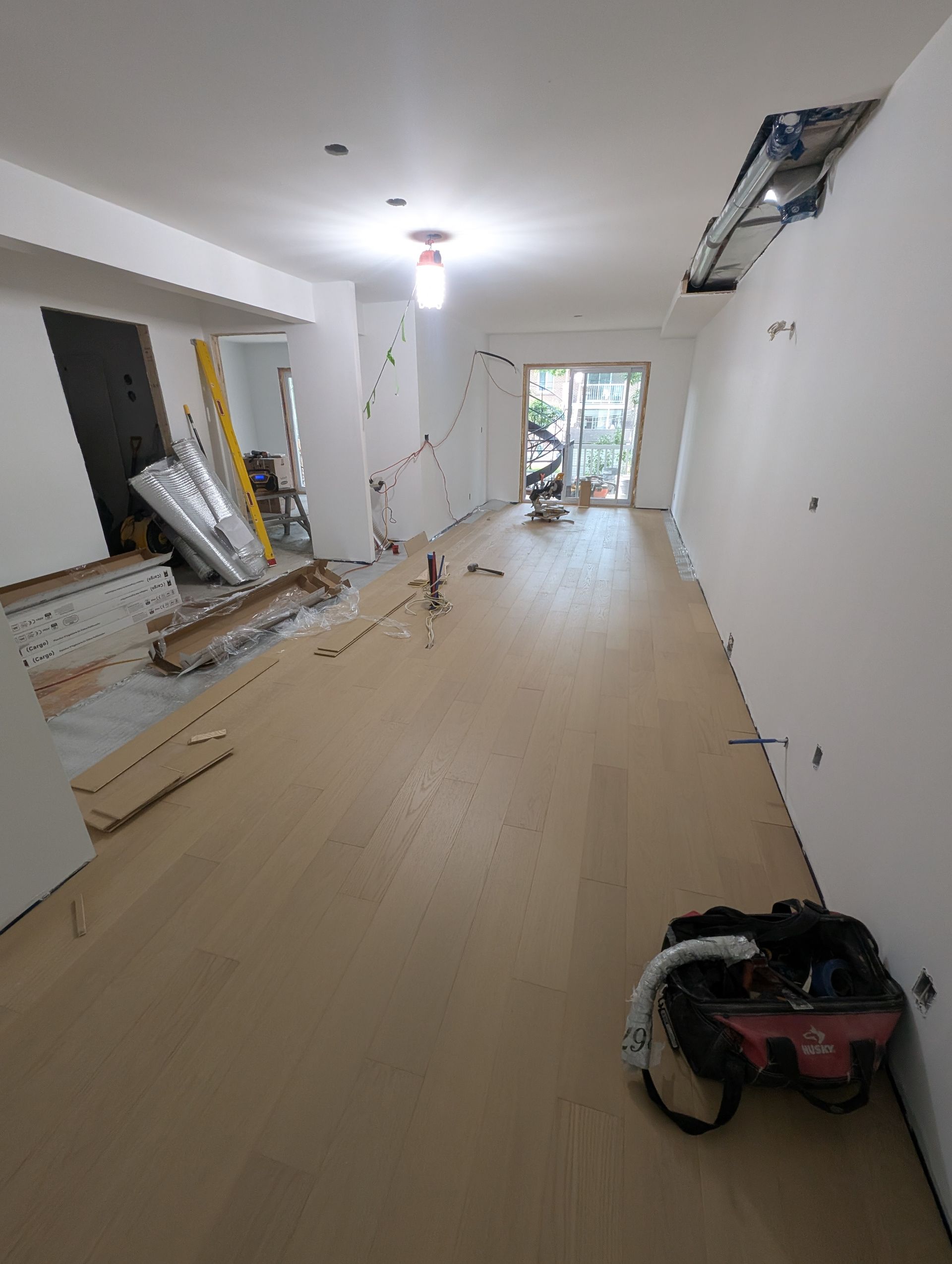 Chambre en cours de rénovation avec nouveau revêtement de sol, murs blancs et plafond apparent.