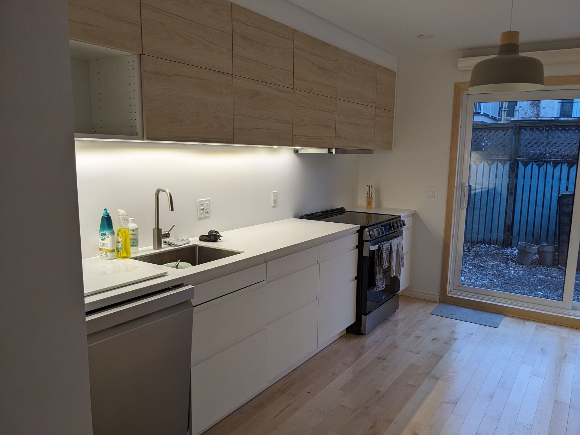 Cuisine moderne avec armoires en bois clair, appareils électroménagers en acier inoxydable et porte-fenêtre coulissante donnant sur le jardin.