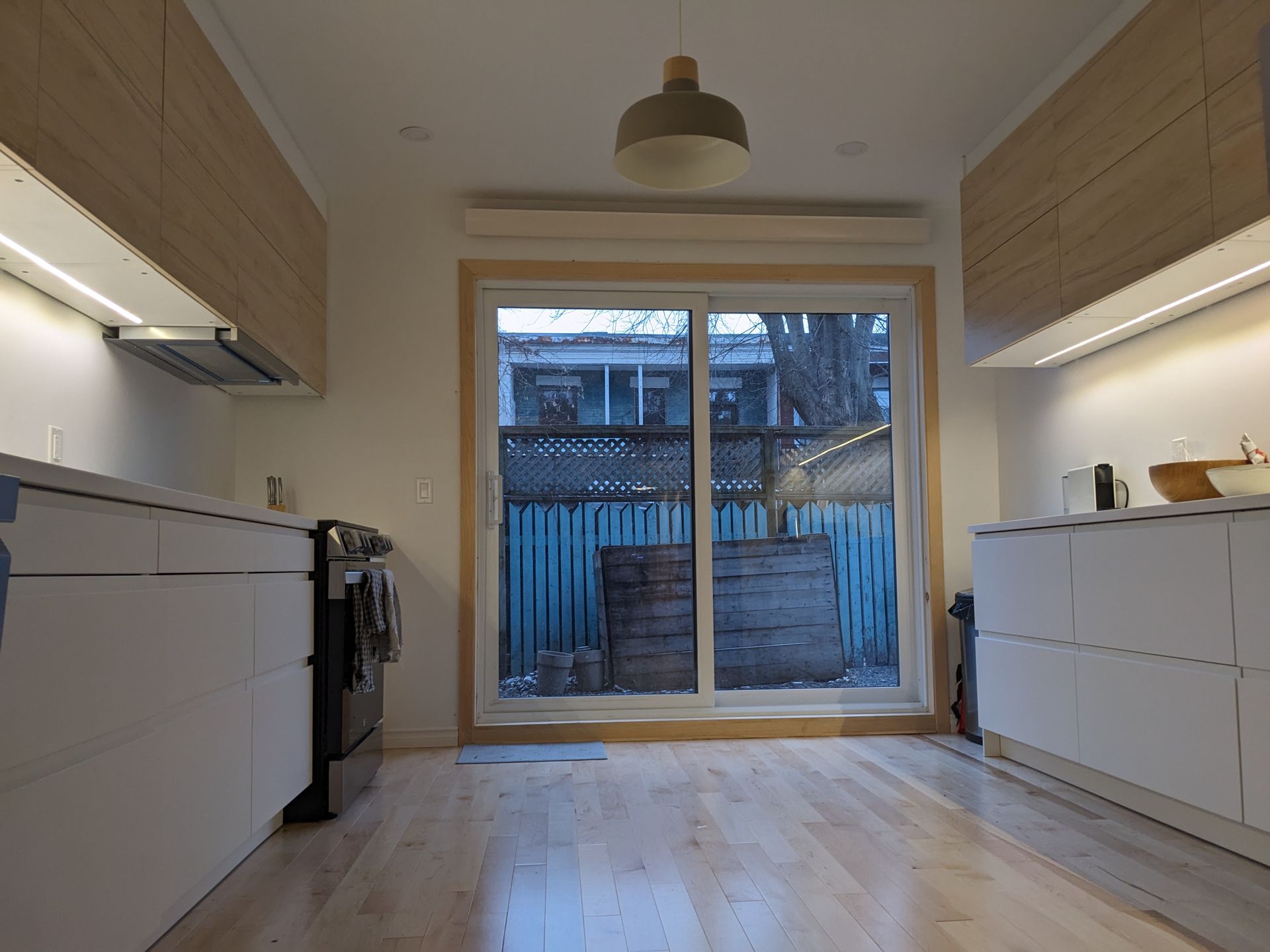 Cuisine moderne avec placards en bois et vue sur le jardin par une porte coulissante en verre.
