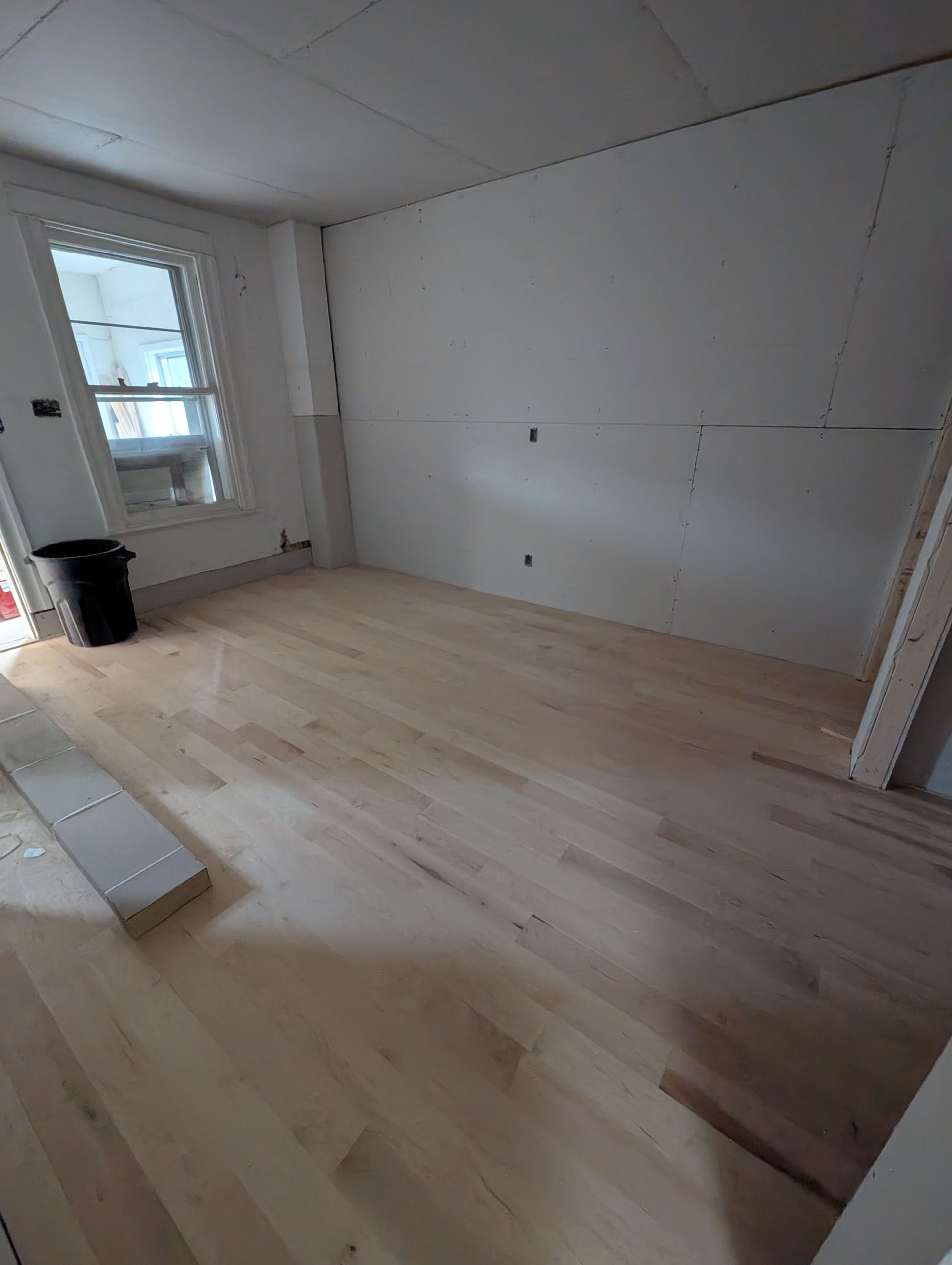 Pièce avec parquet clair récemment installé, murs blancs et fenêtre.