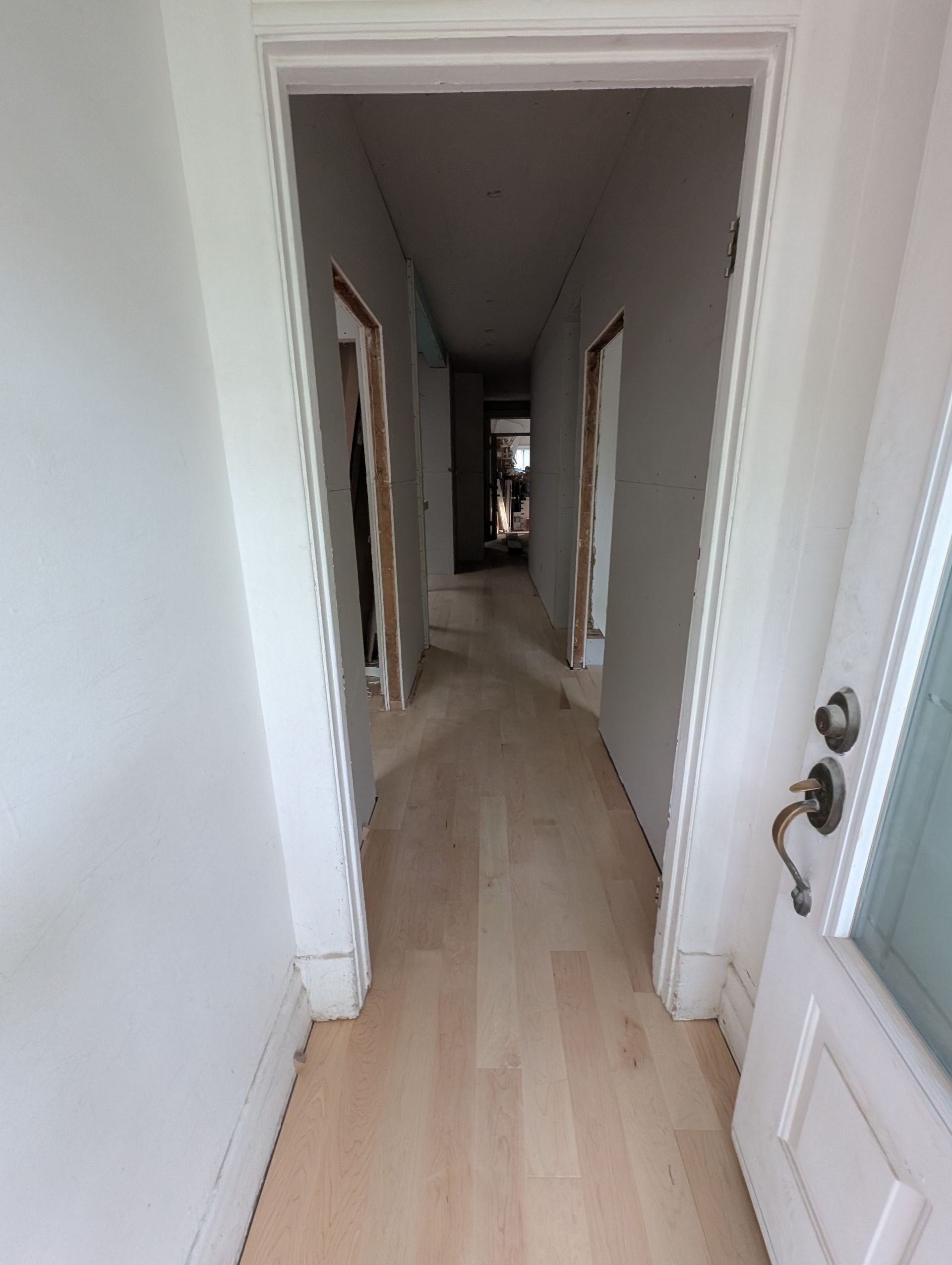 Couloir étroit avec parquet clair, murs blancs et portes ouvertes.