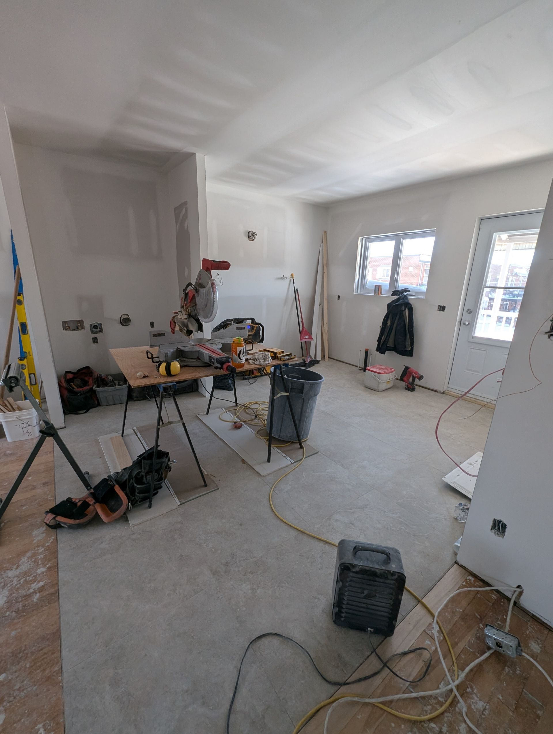 Intérieur d'une pièce en construction, avec des outils, des plaques de plâtre et un établi de scie.