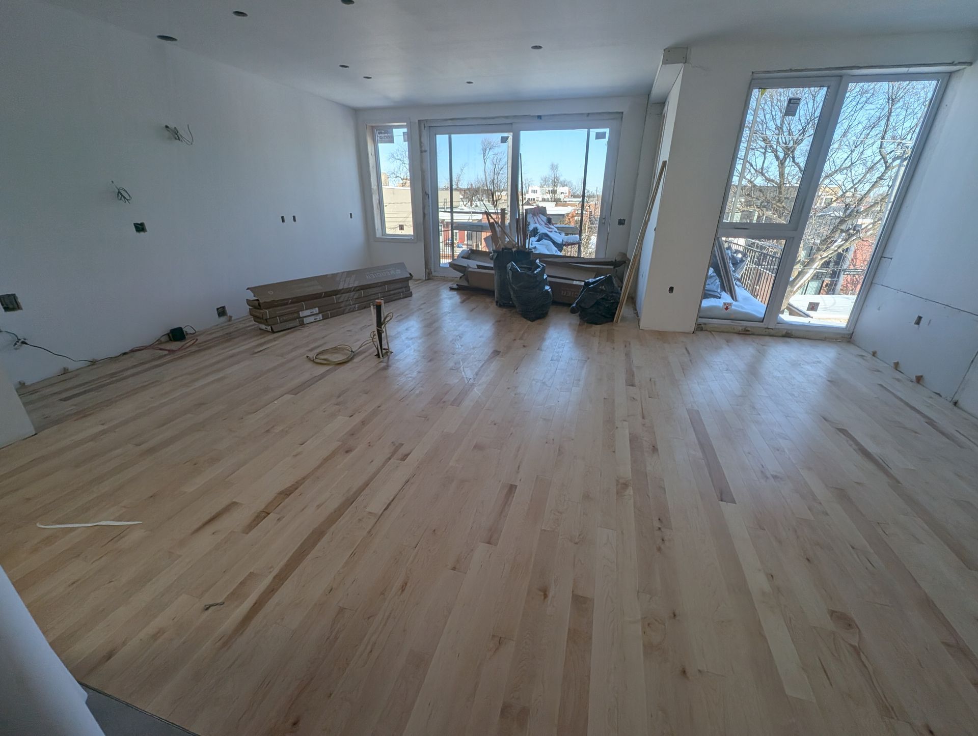 Parquet clair récemment installé dans une pièce aux murs blancs et aux grandes fenêtres, encore en construction.
