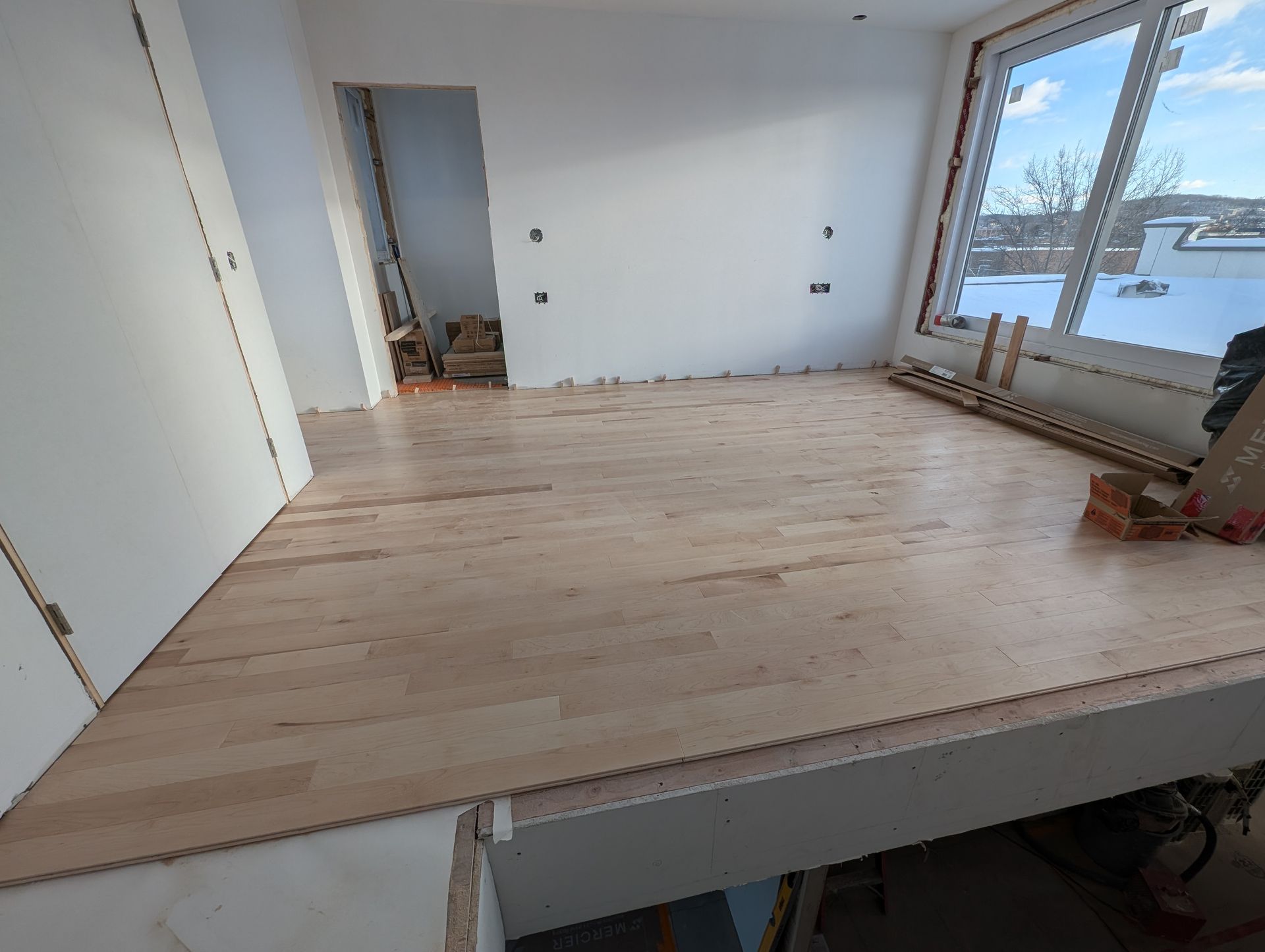 Pièce intérieure avec parquet en bois brut, une grande fenêtre et un cadre de porte.
