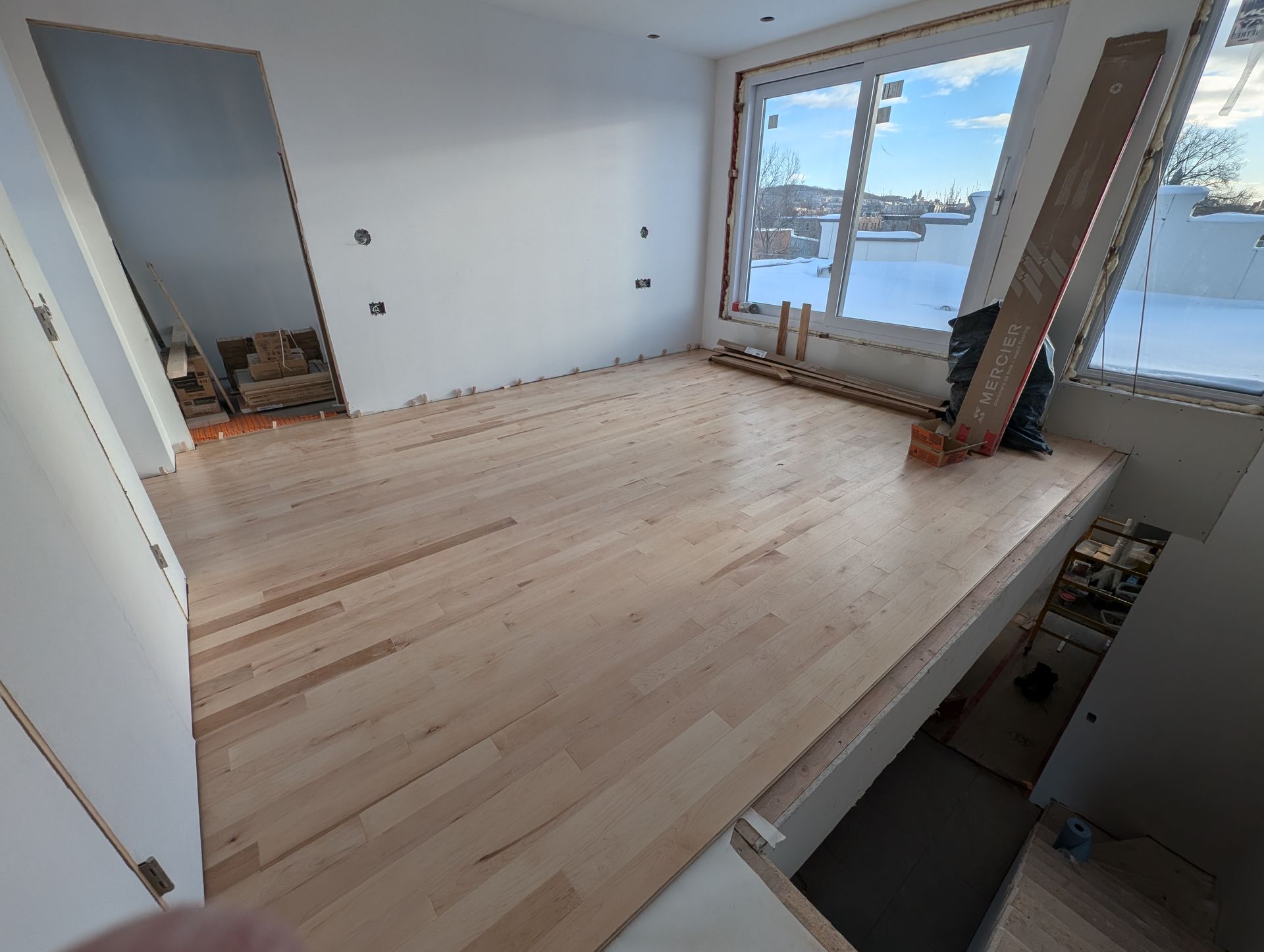 Parquet clair récemment installé dans une pièce avec une grande fenêtre et une estrade.