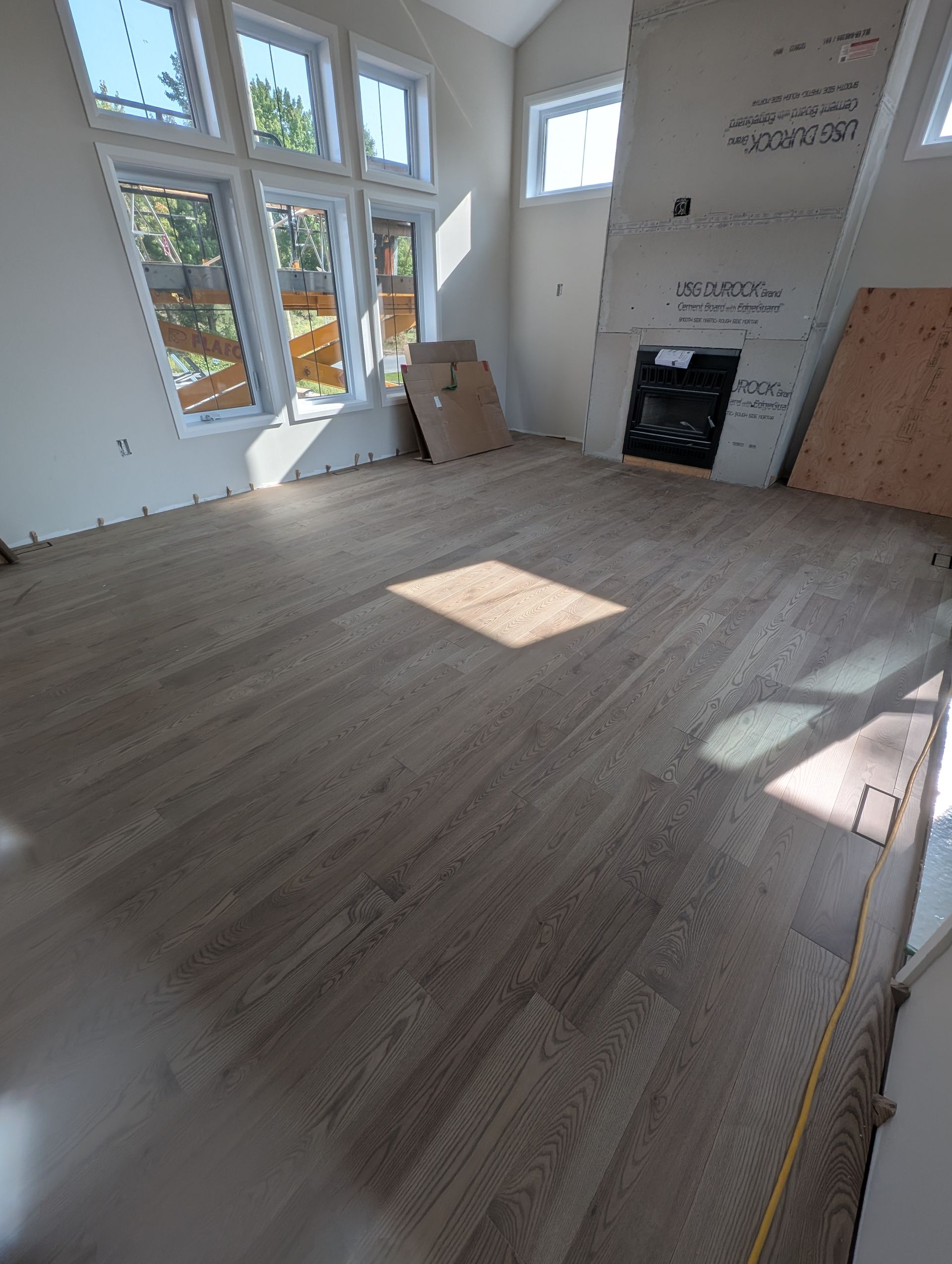 Plancher en bois neuf dans une pièce avec cheminée et hautes fenêtres, en construction.