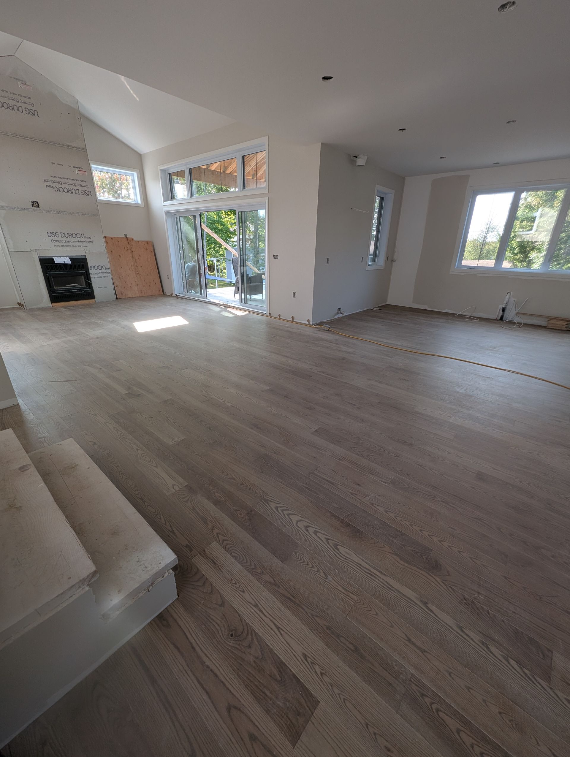Espace de vie récemment rénové avec parquet gris, cheminée et grandes fenêtres.